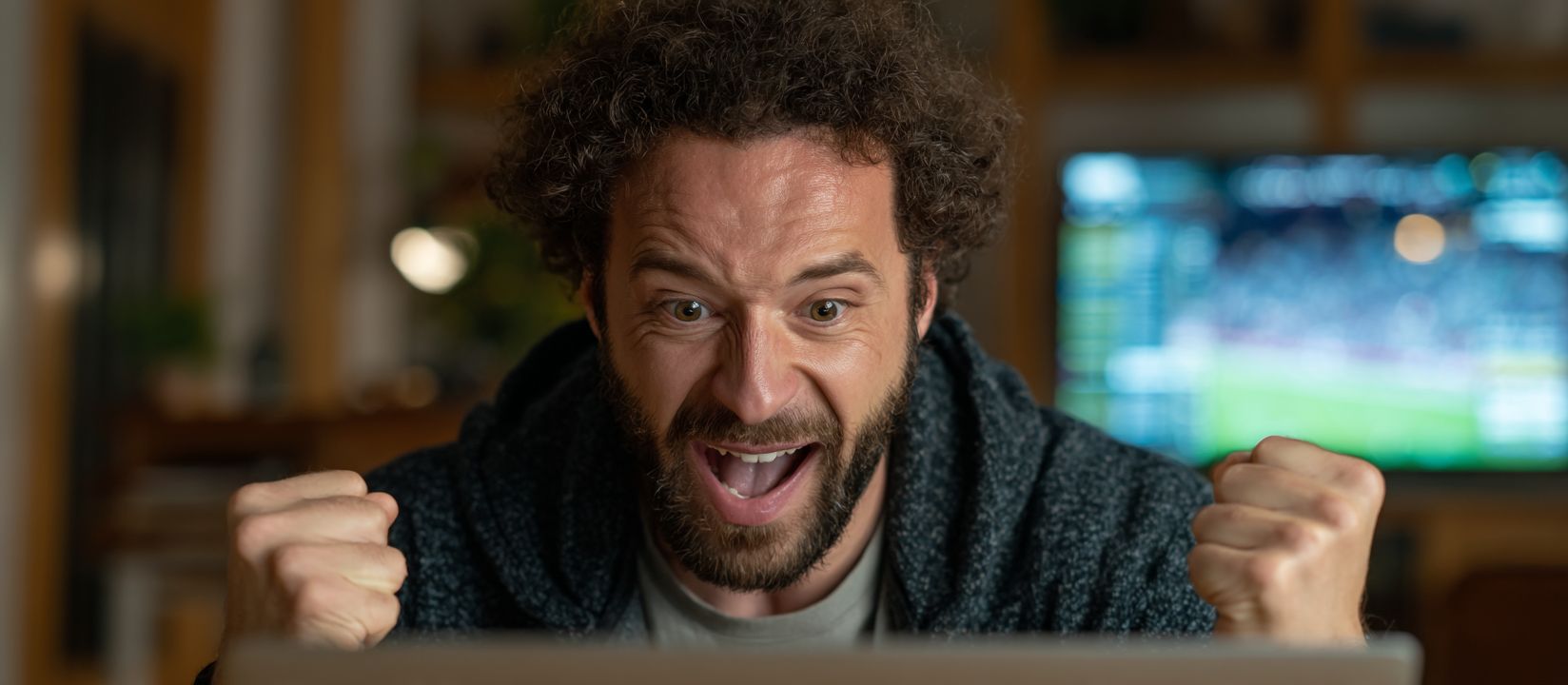 A man with a joyful expression exults in front of the screen as he watches a sports match, symbolising victory in betting on KKK786.